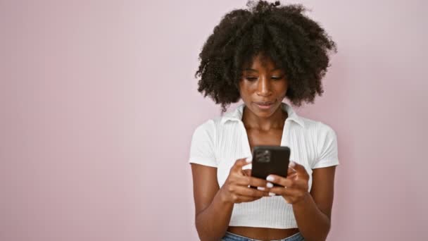 African american woman using smartphone looking to the side over isolated pink background - Footage, Video