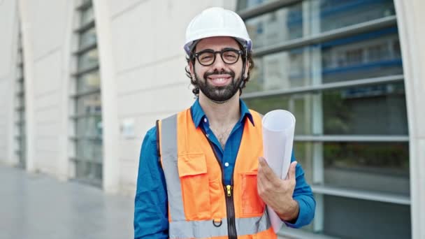 Jonge Spaanse man architect glimlacht vol vertrouwen met blauwdrukken op bouwplaats - Video