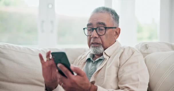 Entspannen Sie sich, mailen Sie und ein älterer Mann mit einem Telefon auf dem heimischen Sofa für Kommunikation und soziale Medien. Technologie, Scrollen und ein älterer Mensch, der Nachrichten auf einer mobilen App oder im Internet online liest. - Filmmaterial, Video