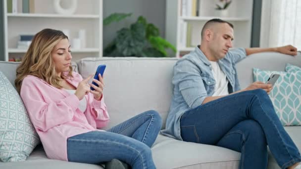 Coppia di uomini e donne che utilizzano smartphone seduti sul divano a casa - Filmati, video