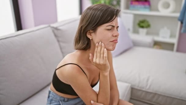 Mladá krásná hispánská žena sedí na pohovce a trpí bolestí zubů doma - Záběry, video