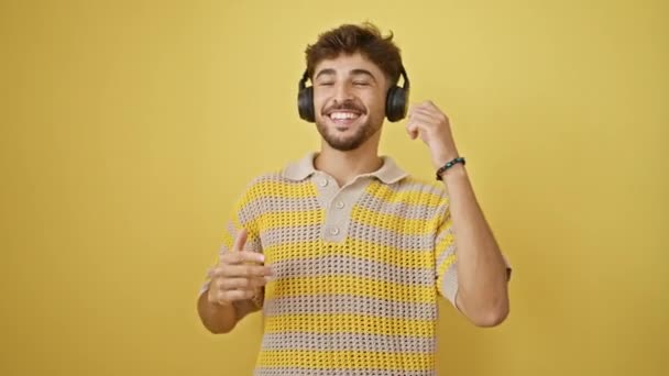 Guay, joven árabe seguro de sí mismo tocando música en sus auriculares. bailando felizmente solo frente a una pared amarilla aislada, irradiando positividad y felicidad. - Metraje, vídeo
