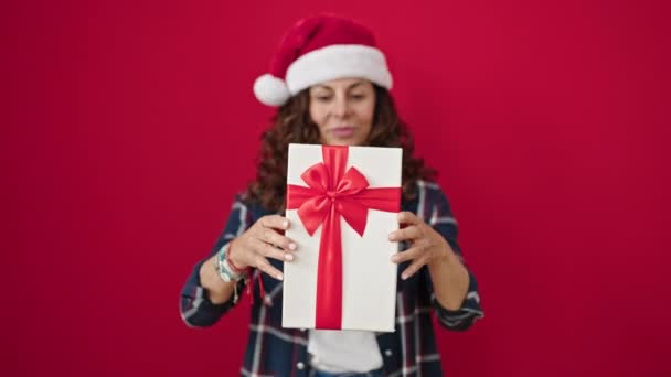 Середньовіччя його жінка посміхається впевнено обіймаючи різдвяний подарунок над ізольованим червоним тлом - Кадри, відео