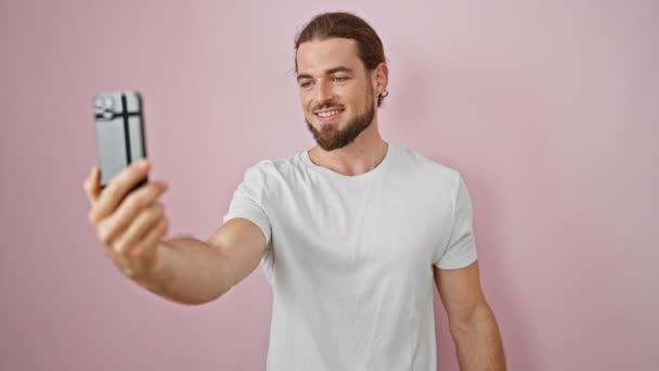 jonge latino man glimlachen zelfverzekerd met video bellen over geïsoleerde roze achtergrond - Video