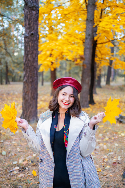 Hello october.  happy trendy woman in red beret and beige coat rejoicing in the city park at sunset. - Photo, Image