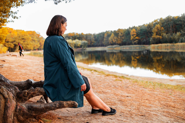 Одинокая женщина сидит на берегу лесного озера. Осенний пейзаж, спокойствие, спокойствие, путешествия. - Фото, изображение