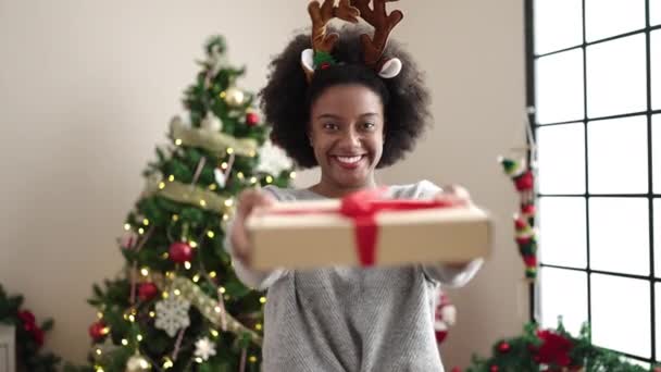 Afroamerikanerin mit Rentierohren hält Weihnachtsgeschenk zu Hause - Filmmaterial, Video