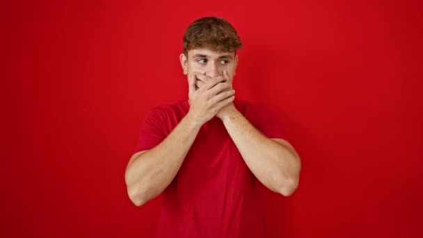 Vrolijke jonge Spaanse man vol vertrouwen bedekken mond met handen over een levendige geïsoleerde rode achtergrond, uitstralen van vertrouwen en geluk - Video