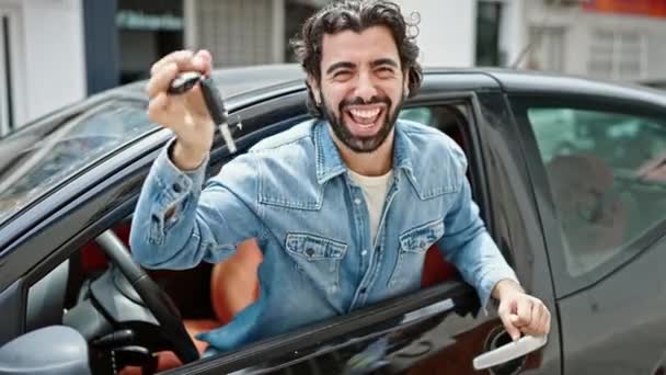 Young hispanic man holding key of new car celebrating at street - Footage, Video
