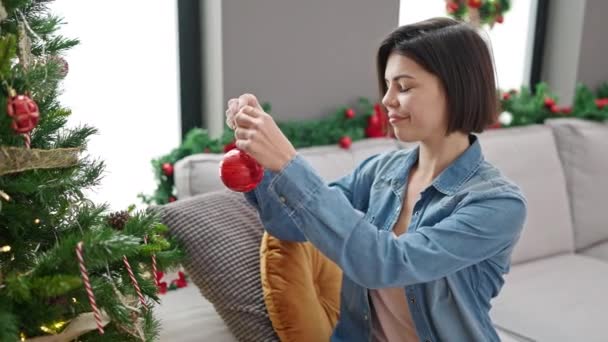 Jovem mulher caucasiana decorando árvore de Natal em casa - Filmagem, Vídeo