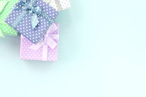 Куча маленьких цветных подарочных коробок с лентами лежит на фиолетовом фоне. Минимализм плоский вид сверху
. - Фото, изображение