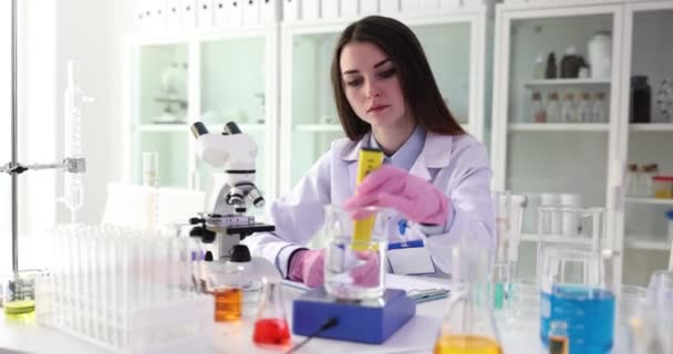 Lo scienziato scrive un rapporto di ricerca e tiene in mano la provetta con un liquido di prova trasparente. Test della qualità dell'acqua - Filmati, video