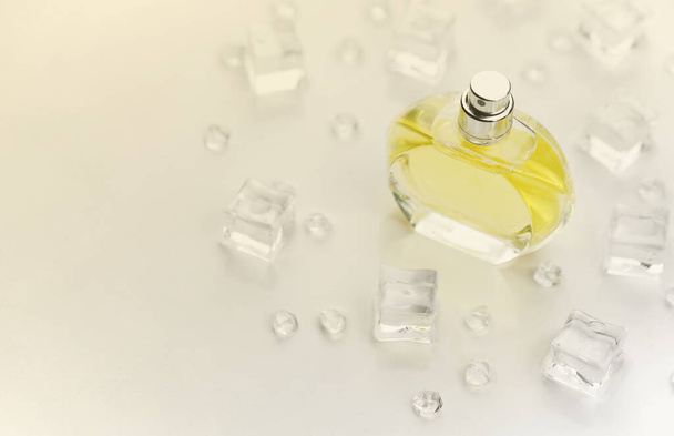 Kadın parfümü sarı şişe, buz küplerinde parfüm şişesinin objektif fotoğrafı ve beyaz masanın üzerindeki su. Yukarıdan bak. Model ürün fotoğrafı, tazelik ve aroma konsepti - Fotoğraf, Görsel