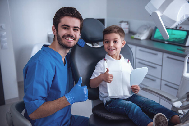 Il bambino è seduto sulla sedia e sorride mentre visita un dentista
 - Foto, immagini
