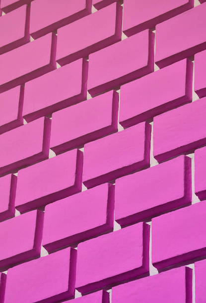 Parede de concreto decorativa com um relevo semelhante a uma grande alvenaria de tijolo pintada em tinta rosa brilhante
 - Foto, Imagem