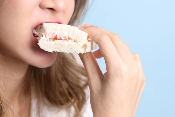 Азиатка ест сэндвичи на голубом фоне. - Фото, изображение