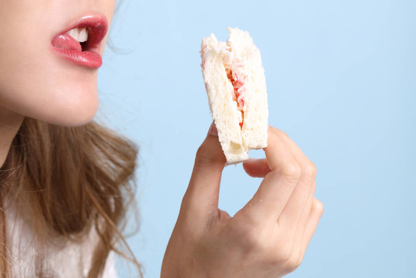 Азиатка ест сэндвичи на голубом фоне. - Фото, изображение