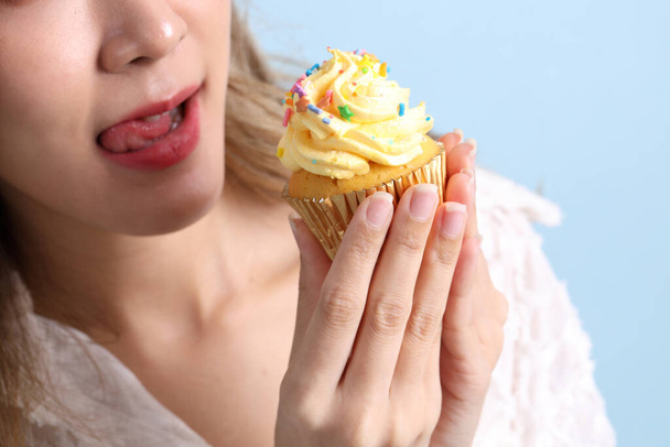 Die Asiatin isst Cupcakes auf blauem Hintergrund. - Foto, Bild