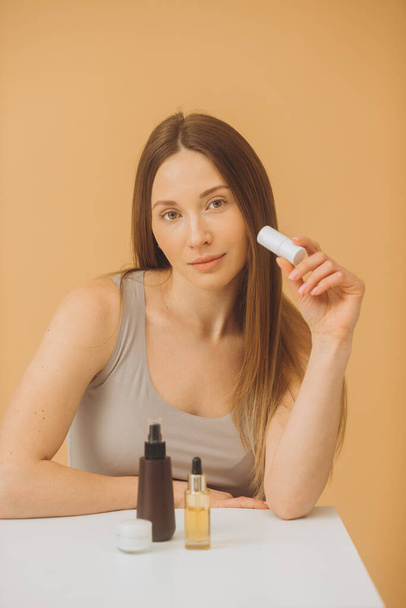 Schöne Frau mit Kosmetikflaschen posiert auf beigem Hintergrund. - Foto, Bild