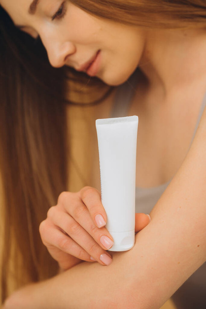 Uma mulher está segurando um tubo com creme cosmético. Retrato de estúdio de uma mulher bonita com um fundo bege. Fechar. - Foto, Imagem