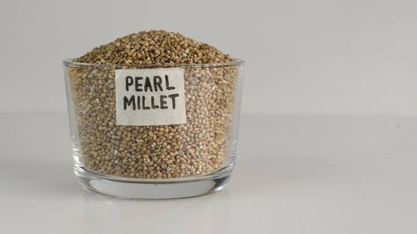 Pearl millet grains in a glass bowl with label on it filled to the brim, showcasing their pearl like natural beauty and healthy nutrition. Ideal for food and agriculture concepts. - Photo, Image