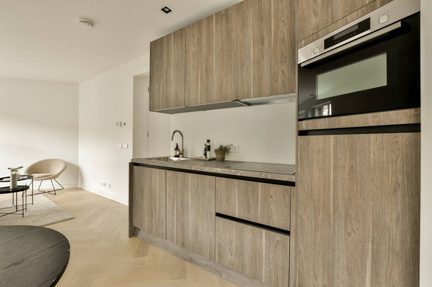 una cocina con armarios de leña y un horno en la pared al lado del espacio de mostrador en la habitación es de color blanco - Foto, Imagen
