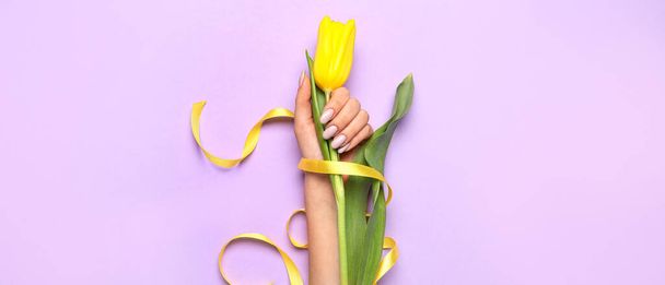 Mano femminile con bella manicure e fiore su sfondo lilla  - Foto, immagini