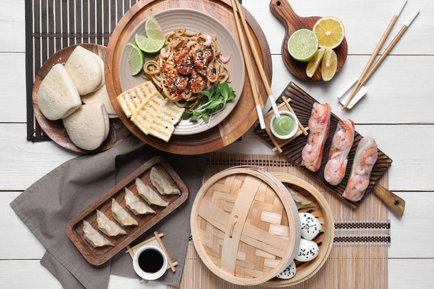 Komposition mit verschiedenen chinesischen Gerichten und Essstäbchen auf hellem Holzgrund - Foto, Bild