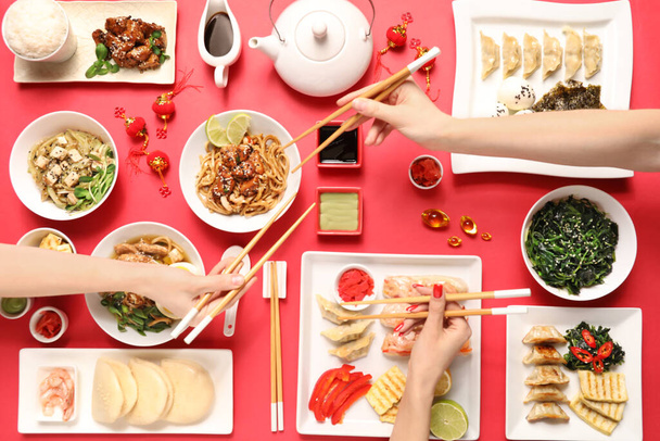 Женские руки с палочками для еды и различными китайскими блюдами на красном фоне - Фото, изображение