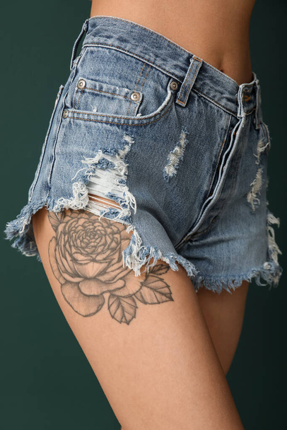 Young woman with tattooed thigh on green background, closeup - Photo, Image