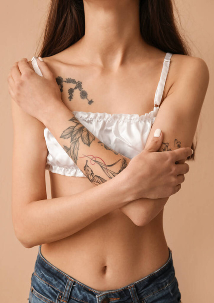 Mujer joven tatuada sobre fondo beige, primer plano - Foto, Imagen