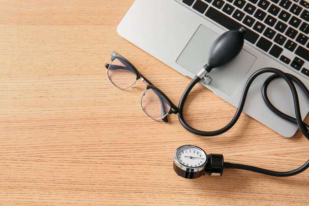 Esfigmomanômetro com laptop e óculos em mesa médica de madeira, close-up - Foto, Imagem