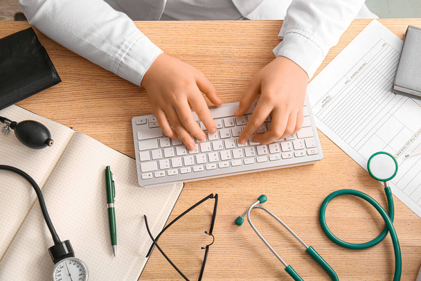 Žena lékař pracuje s počítačem klávesnice na dřevěné lékařské stole, horní pohled - Fotografie, Obrázek