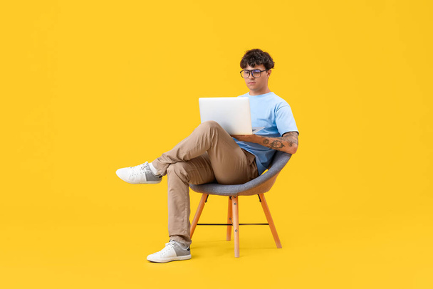 Αρσενικός προγραμματιστής με lap-top που κάθεται στην καρέκλα σε κίτρινο φόντο - Φωτογραφία, εικόνα