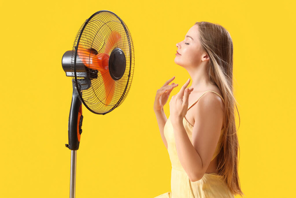 Mladá žena s elektrickým ventilátorem na žlutém pozadí - Fotografie, Obrázek