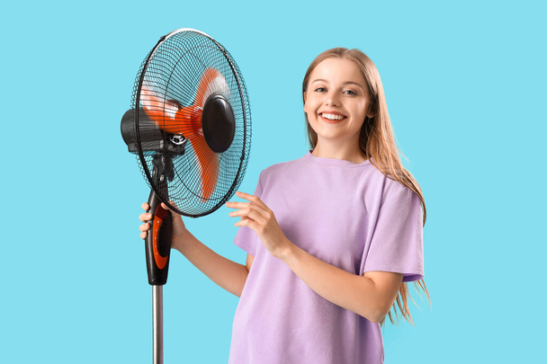 Young woman with electric fan on blue background - Photo, Image