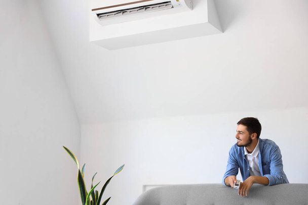 Nuori mies ilmastointilaite kaukosäädin kotona - Valokuva, kuva