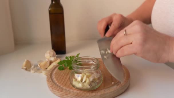 vrouw bewaart knoflookteentjes met kruiden in olie in glazen pot - Video