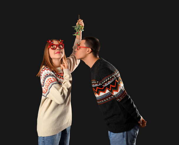 Young couple kissing under mistletoe branch on dark background - Photo, Image