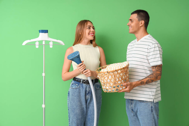 Junges Paar mit Dampfer und Wäschekorb auf grünem Hintergrund - Foto, Bild