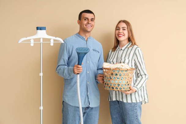 Junges Paar mit Dampfer und Wäschekorb auf beigem Hintergrund - Foto, Bild