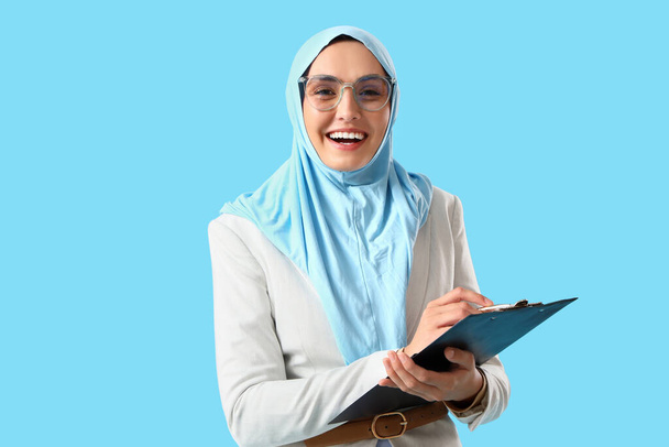 Νεαρή μουσουλμάνα επιχειρηματίας με πρόχειρο σε μπλε φόντο - Φωτογραφία, εικόνα