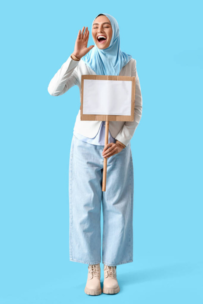 Mulher muçulmana elegante com placa em branco no fundo azul - Foto, Imagem