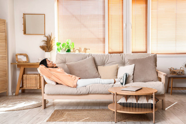 Young Asian woman in stylish hoodie sleeping on sofa at home - Фото, зображення