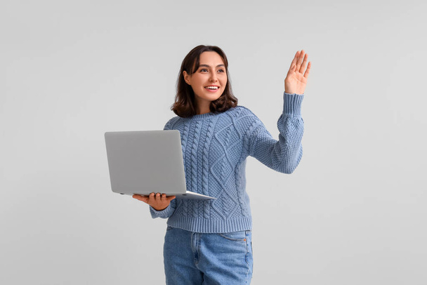 Молодая женщина в теплом свитере с ноутбуком на светлом фоне - Фото, изображение