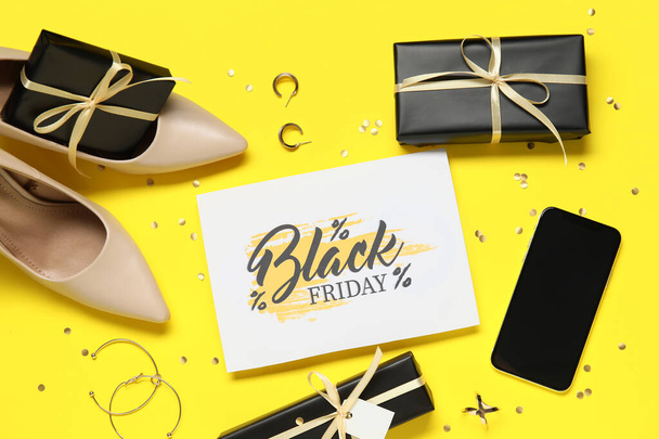 Tarjeta de felicitación de venta Viernes Negro con teléfono móvil, zapatos, joyas y cajas de regalo sobre fondo amarillo - Foto, imagen