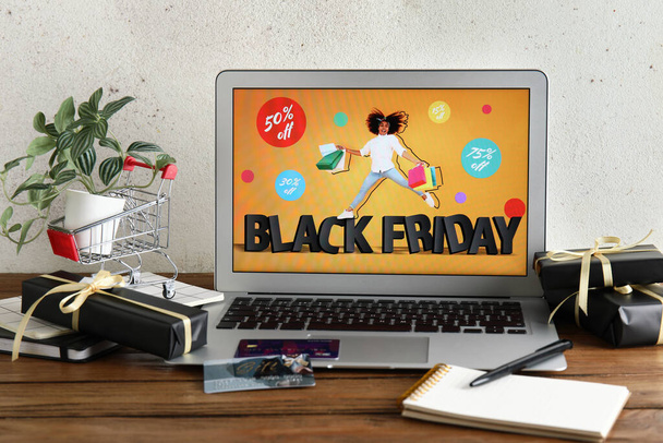 Laptop mit Black-Friday-Verkaufswerbung, Kreditkarten und Geschenkboxen auf Holztisch - Foto, Bild