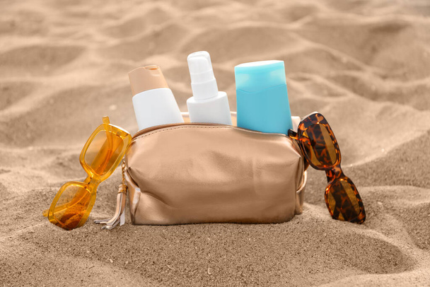 Kosmetiktasche mit Flaschen Sonnencreme und Sonnenbrille auf sandigem Hintergrund - Foto, Bild