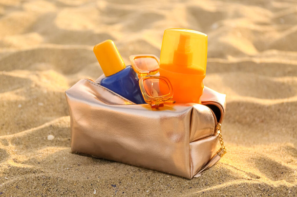 Güneş kremi şişeleri ve kumlu arka planda güneş gözlüğü olan kozmetik çanta. - Fotoğraf, Görsel