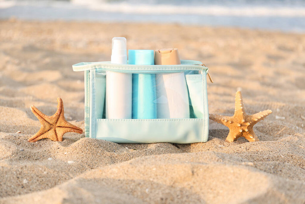 Καλλυντική τσάντα με μπουκαλάκια αντηλιακής κρέμας και αστερίες στην άμμο - Φωτογραφία, εικόνα